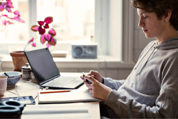 Gutt ved skrivebord med laptop, telefon og skriveblokk