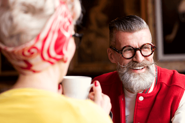 Mann med skjegg og briller i rød jakke smiler i selskap med en dame