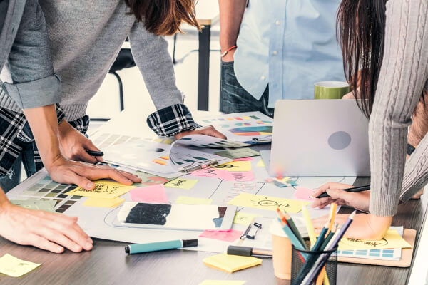 Skrivebord med notater og lapper, personer som arbeider